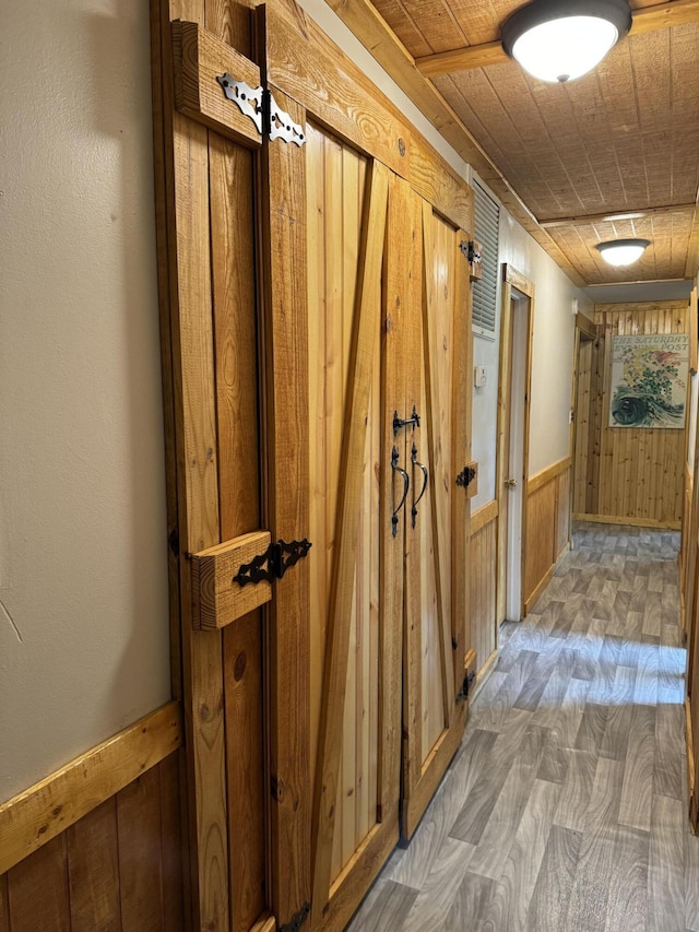 hallway featuring wooden walls, wood finished floors, and a wainscoted wall