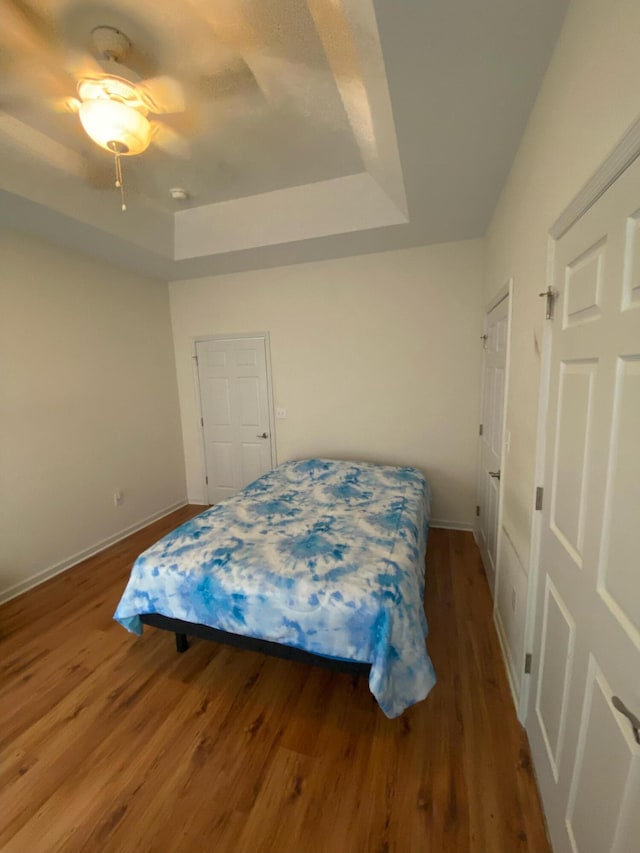 bedroom featuring ceiling fan, a raised ceiling, and wood-type flooring