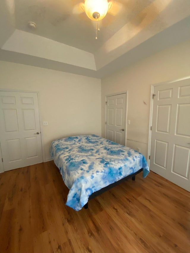 bedroom featuring ceiling fan, a raised ceiling, and wood finished floors