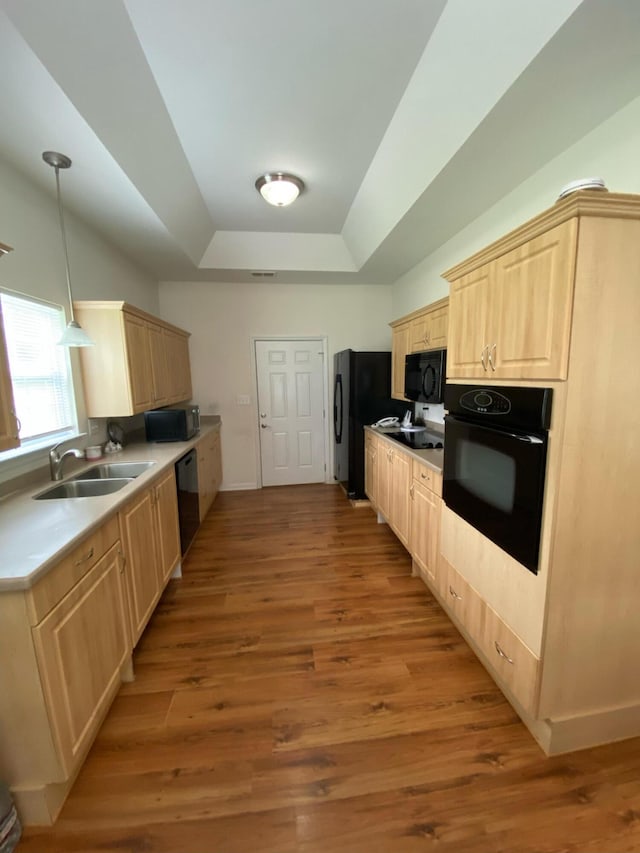 kitchen featuring light brown cabinets, light wood-style flooring, black appliances, a raised ceiling, and a sink