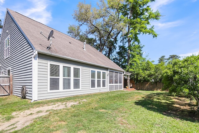 rear view of property featuring a lawn, roof with shingles, fence, and a sunroom