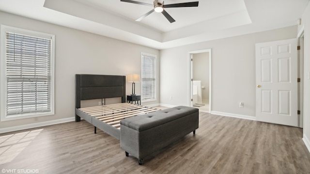 bedroom with ensuite bathroom, a raised ceiling, multiple windows, and hardwood / wood-style floors