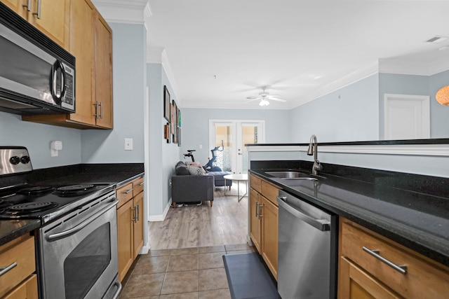 kitchen with stainless steel appliances, dark stone counters, sink, ornamental molding, and light hardwood / wood-style flooring