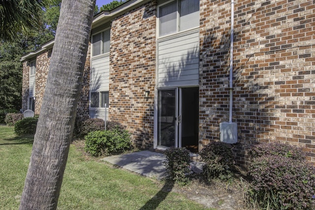 view of exterior entry with brick siding and a yard