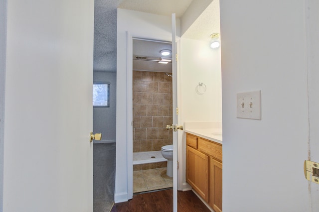 bathroom featuring vanity, wood-type flooring, tiled shower, toilet, and a textured ceiling