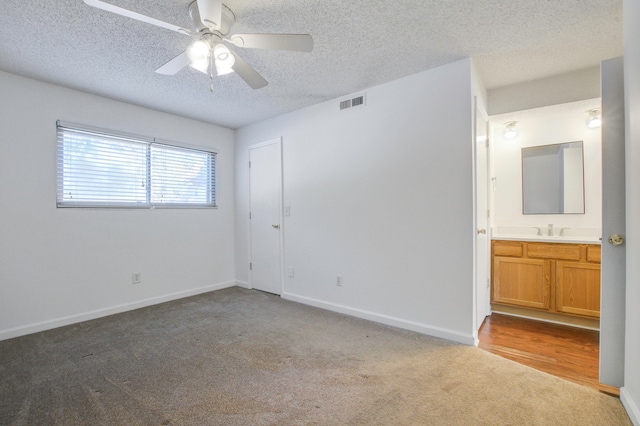 empty room with a textured ceiling, ceiling fan, sink, and light colored carpet