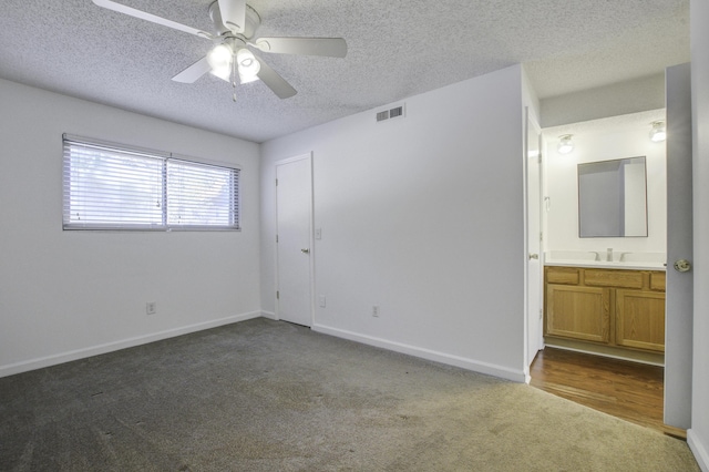 unfurnished bedroom featuring a sink, a textured ceiling, connected bathroom, dark colored carpet, and visible vents