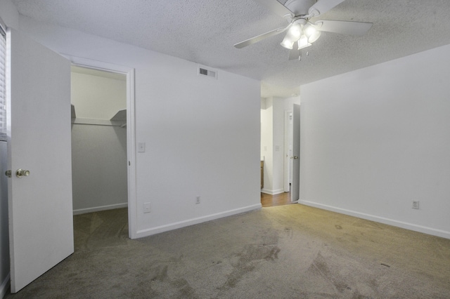 unfurnished bedroom featuring carpet, visible vents, a walk in closet, a textured ceiling, and ceiling fan