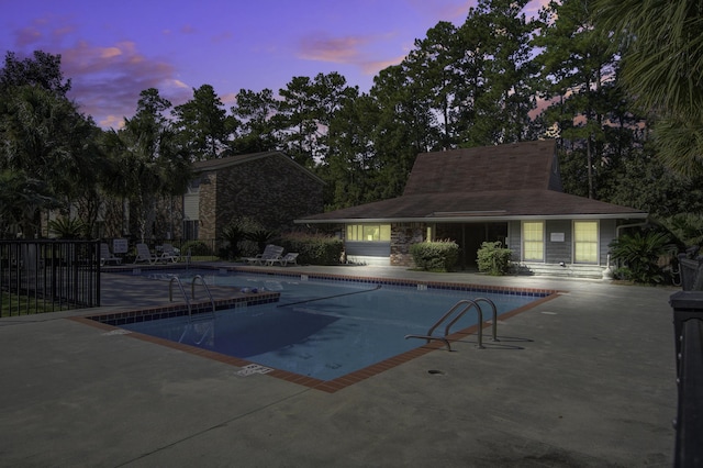 pool at dusk featuring fence, a community pool, and a patio