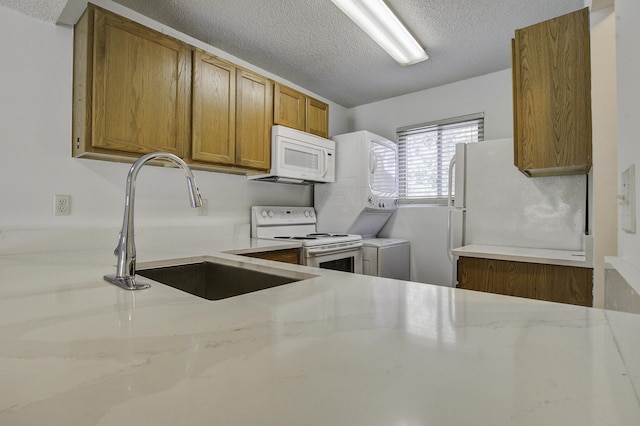 kitchen featuring a sink, a textured ceiling, white appliances, light stone countertops, and brown cabinetry