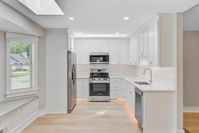 kitchen with appliances with stainless steel finishes, a sink, light countertops, decorative backsplash, and a skylight