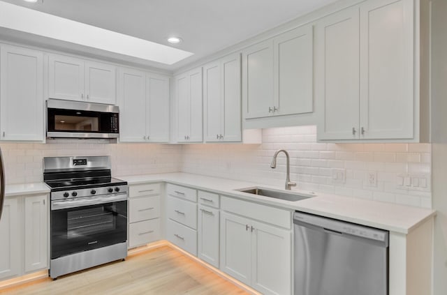 kitchen with appliances with stainless steel finishes, a sink, light countertops, decorative backsplash, and recessed lighting