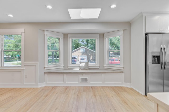unfurnished dining area featuring light wood finished floors, a skylight, wainscoting, recessed lighting, and a decorative wall