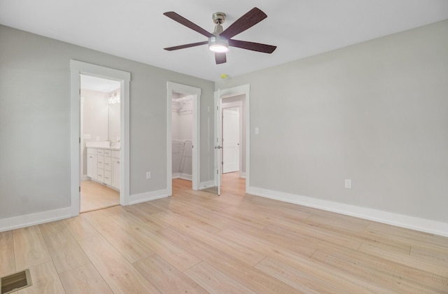 unfurnished bedroom with a spacious closet, a closet, light wood-style floors, baseboards, and ensuite bathroom