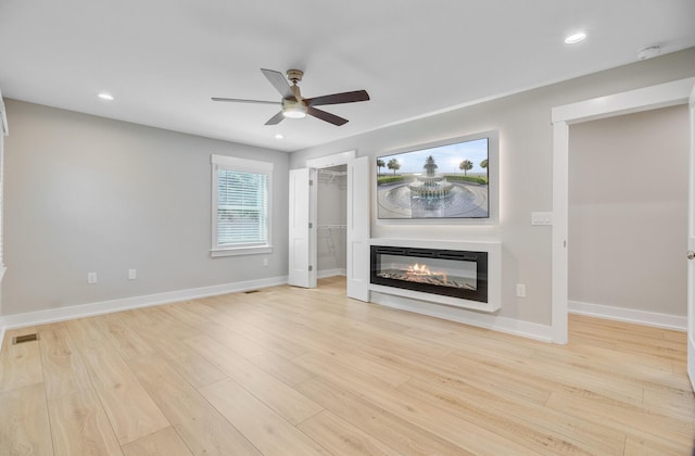 unfurnished living room featuring ceiling fan, light wood finished floors, baseboards, a glass covered fireplace, and recessed lighting
