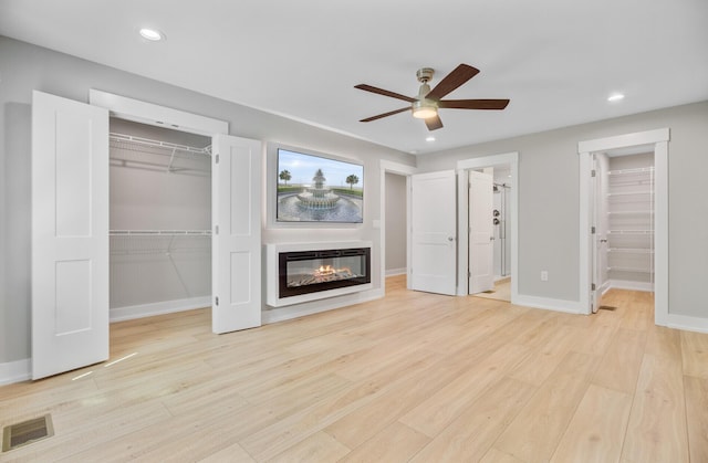 unfurnished living room featuring ceiling fan, light wood finished floors, baseboards, a glass covered fireplace, and recessed lighting