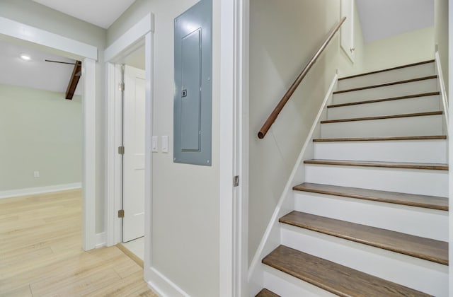 stairway with electric panel, wood finished floors, and baseboards