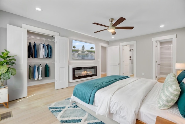 bedroom with a closet, light wood finished floors, recessed lighting, a glass covered fireplace, and a ceiling fan
