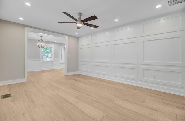 spare room featuring a decorative wall, light wood finished floors, ceiling fan, a chandelier, and recessed lighting