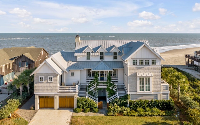 view of front of home with driveway, metal roof, a water view, an attached garage, and a view of the beach