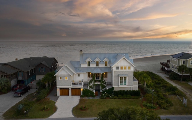 view of front facade with metal roof, a garage, a beach view, a water view, and driveway