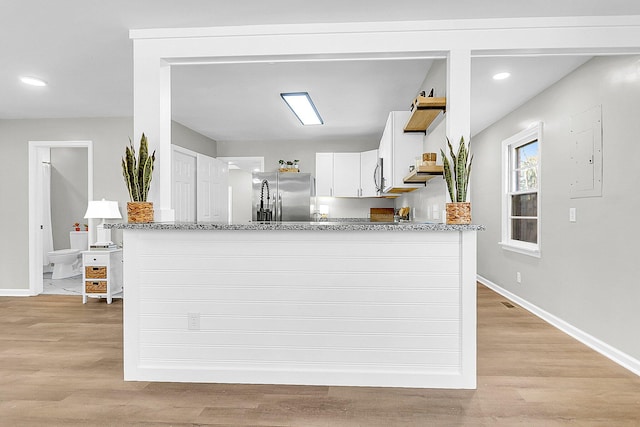 kitchen with white cabinets, light hardwood / wood-style flooring, stainless steel fridge, light stone counters, and kitchen peninsula