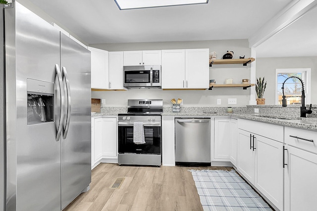 kitchen with sink, stainless steel appliances, light stone counters, light hardwood / wood-style floors, and white cabinets