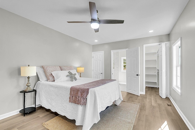 bedroom with ceiling fan, light hardwood / wood-style floors, a spacious closet, and multiple windows