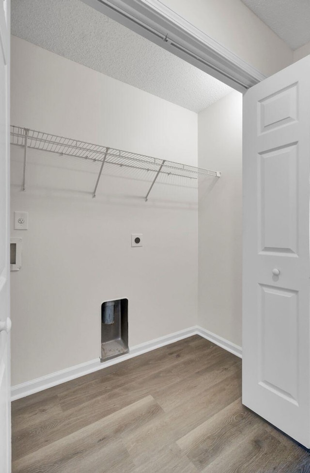 clothes washing area with electric dryer hookup, hardwood / wood-style flooring, and a textured ceiling