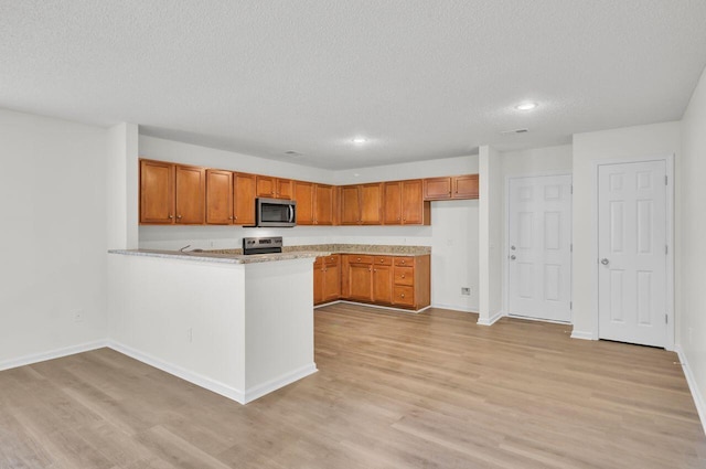 kitchen with a textured ceiling, stainless steel appliances, light hardwood / wood-style floors, and kitchen peninsula