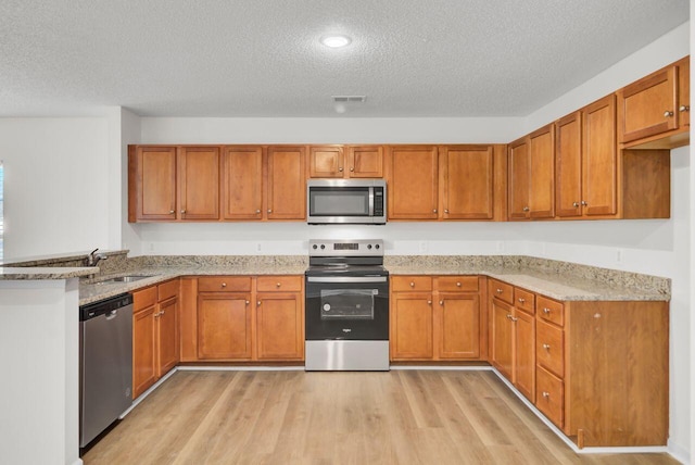 kitchen with sink, appliances with stainless steel finishes, light stone counters, light hardwood / wood-style floors, and a textured ceiling