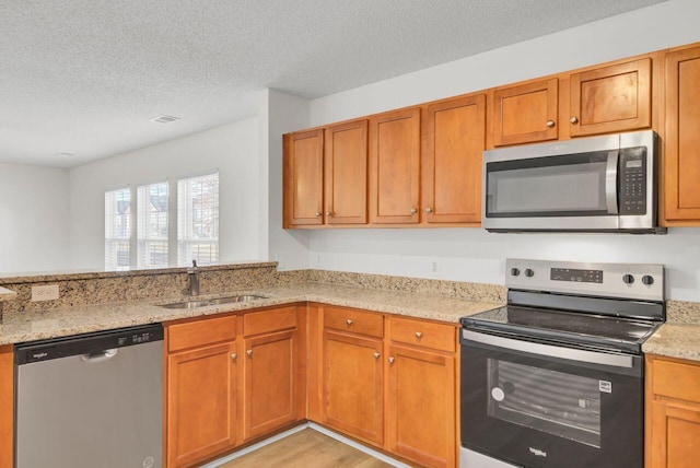 kitchen with light stone counters, appliances with stainless steel finishes, sink, and a textured ceiling