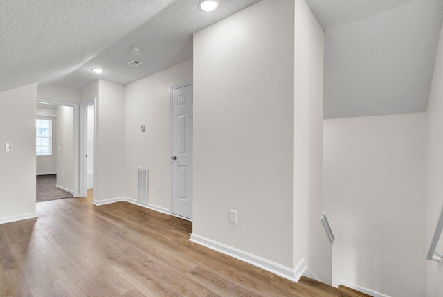 interior space featuring lofted ceiling, a textured ceiling, and light hardwood / wood-style flooring