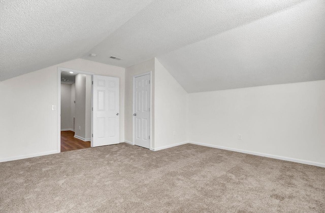 bonus room featuring dark colored carpet, lofted ceiling, and a textured ceiling