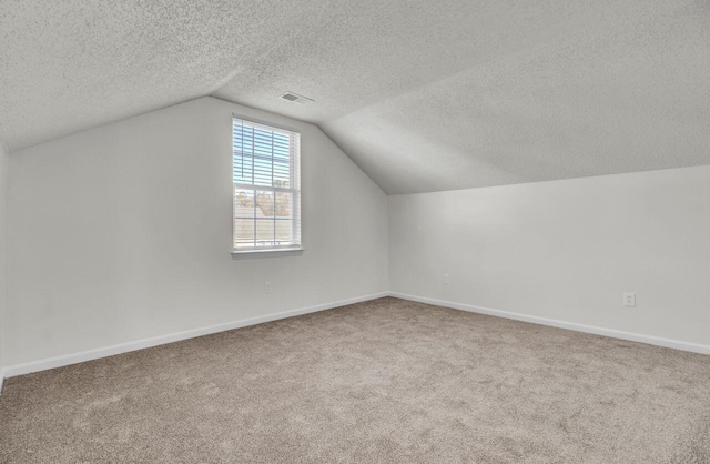 additional living space featuring vaulted ceiling, a textured ceiling, and carpet