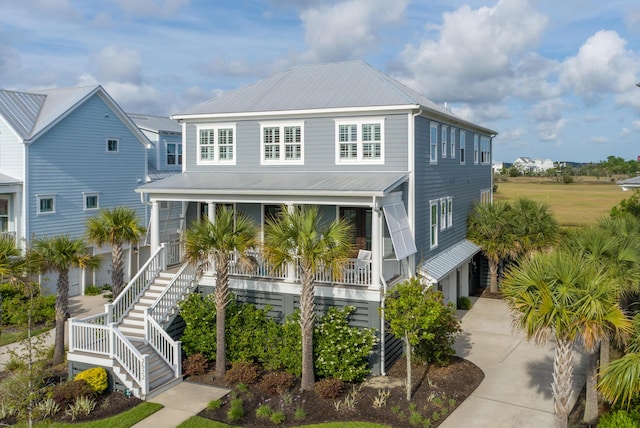coastal home featuring metal roof, covered porch, stairway, and concrete driveway