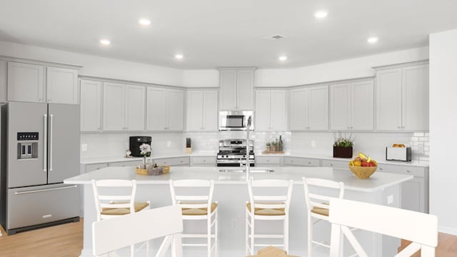 kitchen featuring decorative backsplash, a kitchen bar, light wood-type flooring, stainless steel appliances, and a kitchen island with sink