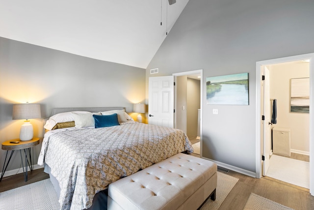 bedroom with connected bathroom, light hardwood / wood-style floors, and high vaulted ceiling