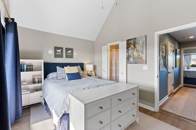 bedroom featuring high vaulted ceiling, light hardwood / wood-style floors, and ensuite bath