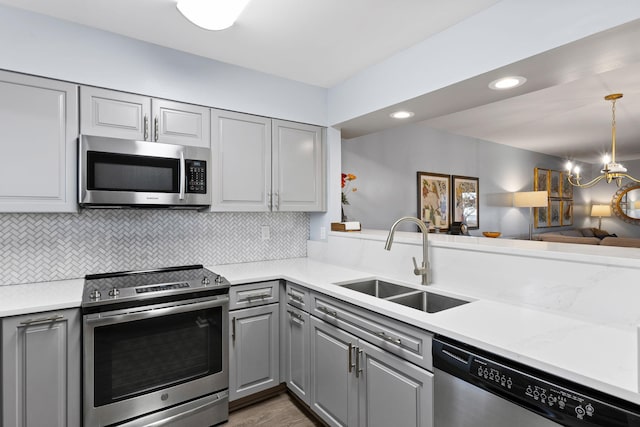 kitchen with sink, a notable chandelier, gray cabinets, appliances with stainless steel finishes, and tasteful backsplash