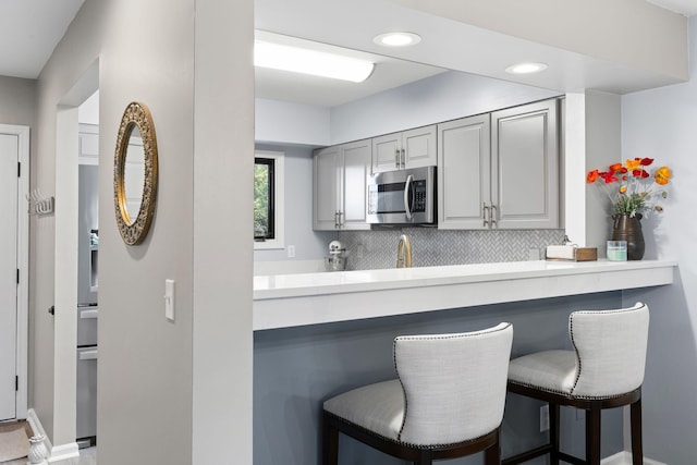 kitchen featuring gray cabinetry, tasteful backsplash, a breakfast bar, and kitchen peninsula