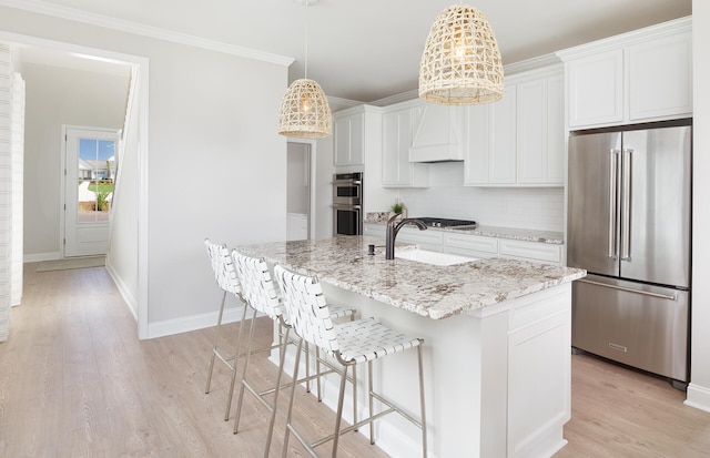 kitchen with light stone countertops, appliances with stainless steel finishes, light wood-type flooring, a kitchen island with sink, and white cabinetry