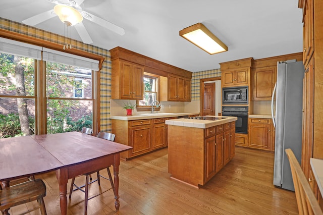 kitchen with light hardwood / wood-style flooring, sink, black appliances, a center island, and ceiling fan