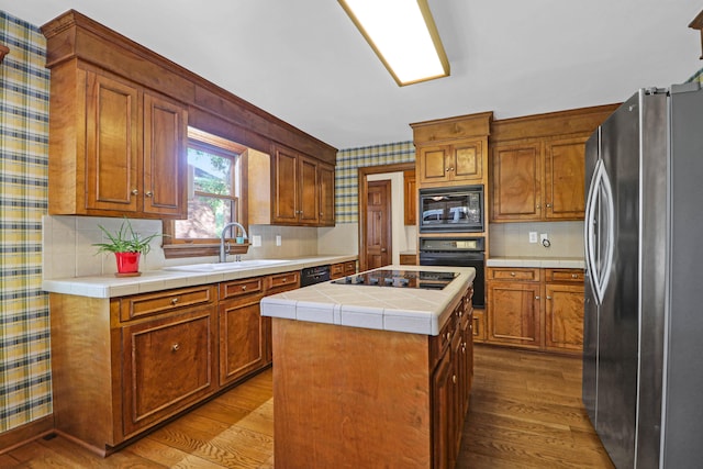 kitchen featuring a kitchen island, light wood-type flooring, black appliances, tile counters, and sink