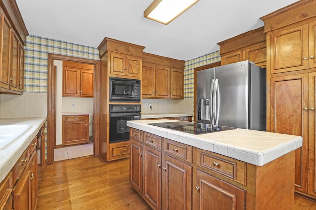 kitchen featuring tile countertops, black appliances, light wood-type flooring, and a kitchen island