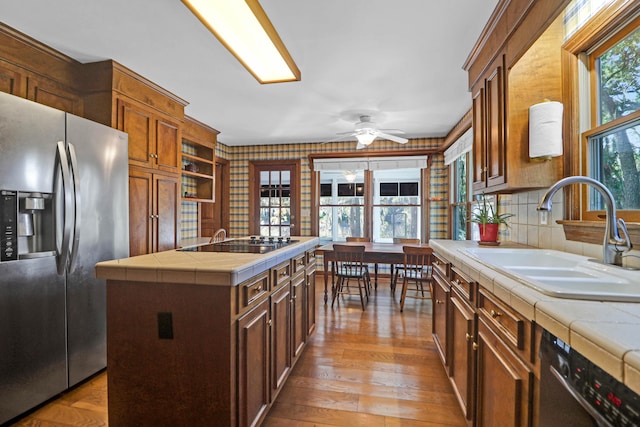 kitchen with tile countertops, sink, a center island, light wood-type flooring, and appliances with stainless steel finishes