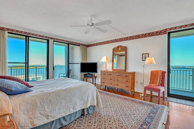 bedroom with hardwood / wood-style floors, ceiling fan, a textured ceiling, access to exterior, and a water view