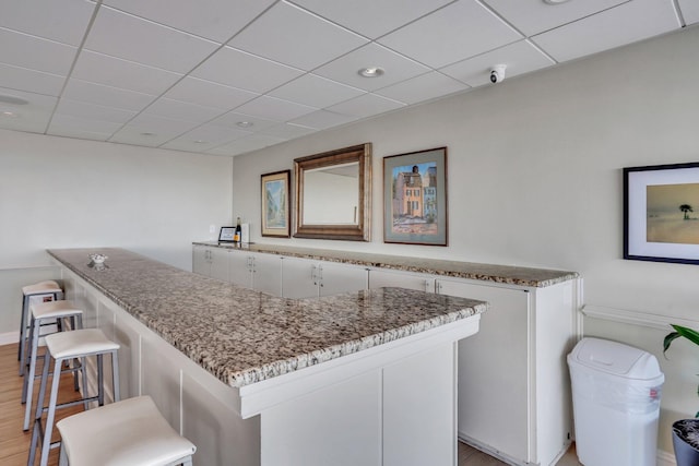 kitchen with light stone countertops, a breakfast bar, white cabinets, and light hardwood / wood-style flooring