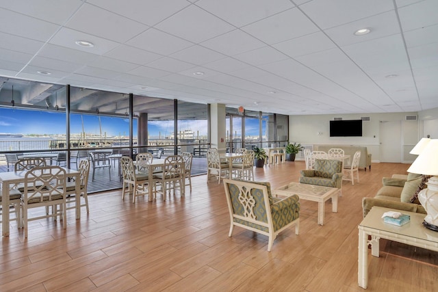 living room with a water view, a paneled ceiling, floor to ceiling windows, and light wood-type flooring