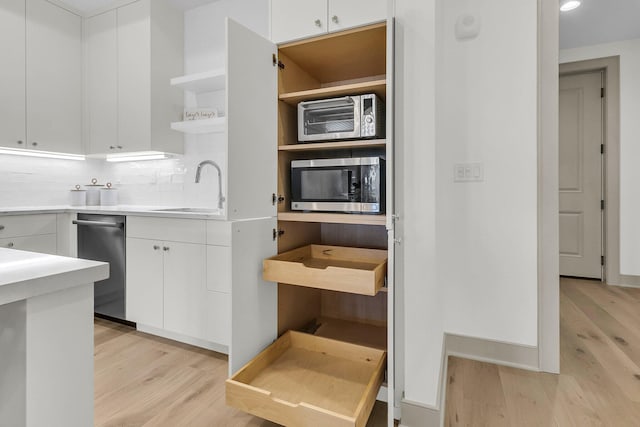 kitchen with light hardwood / wood-style floors, white cabinets, tasteful backsplash, and sink